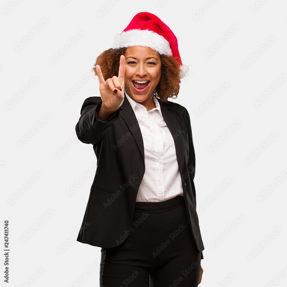 Young business black woman wearing a chirstmas santa hat doing a rock gesture Young business black woman wearing a chirstmas santa hat doing a rock gesture