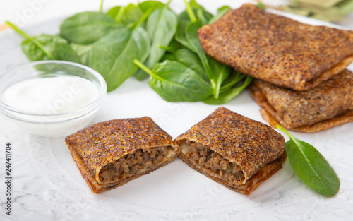 Russian pancakes with meat with spinach leaves and sour cream