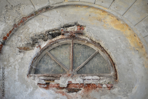 Very old and weatherbeaten semicircular metal window in ancient grey stone wall