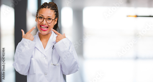 Portrait of a young black doctor woman smiles, pointing mouth, concept of perfect teeth, white teeth, has a cheerful and jovial attitude © Asier