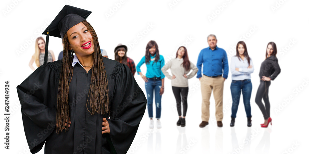 Young graduated black woman wearing braids with hands on hips, standing, relaxed and smiling, very positive and cheerful