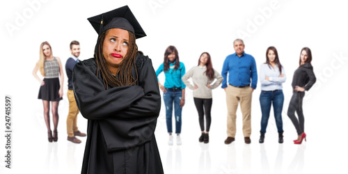 Young graduated black woman wearing braids doubting and shrugging shoulders, concept of indecision and insecurity, uncertain about something