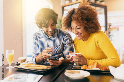 Young modern couple at cafe, she is drinking a tea and he is drinking a coffee, he is showing her something funny in his mobile phone. They are happy and feel comfortable.