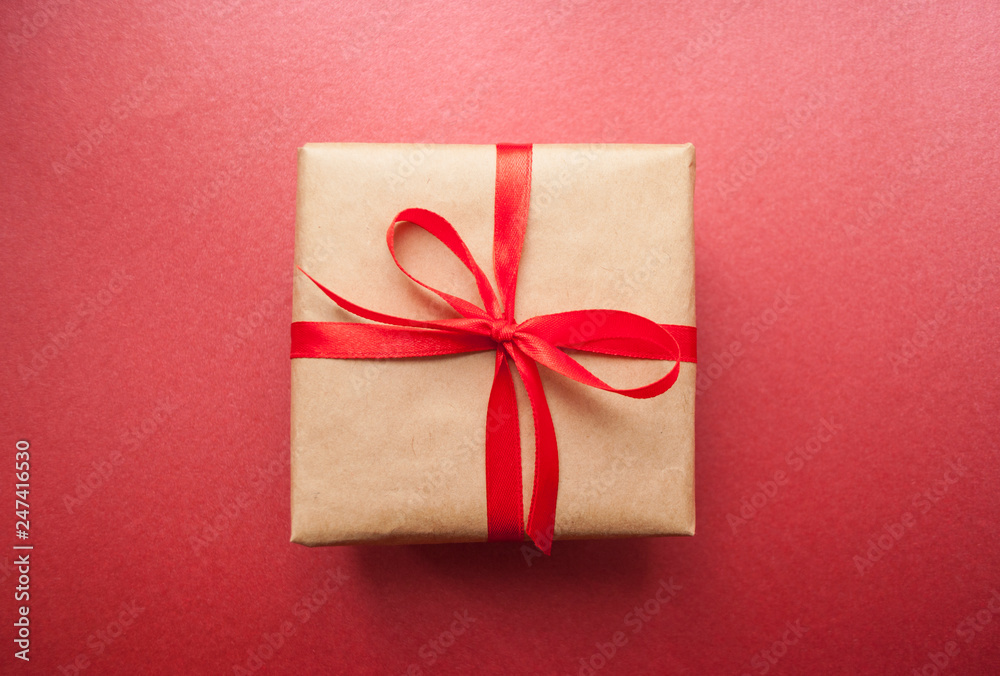 Gift box wrapped in brown colored craft paper and tied with red bow on dark red background. Gift box wrapped in brown colored craft paper and tied with red bow on dark red background.