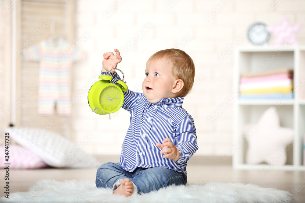 Baby boy with alarm clock sitting at home Baby boy with alarm clock sitting at home