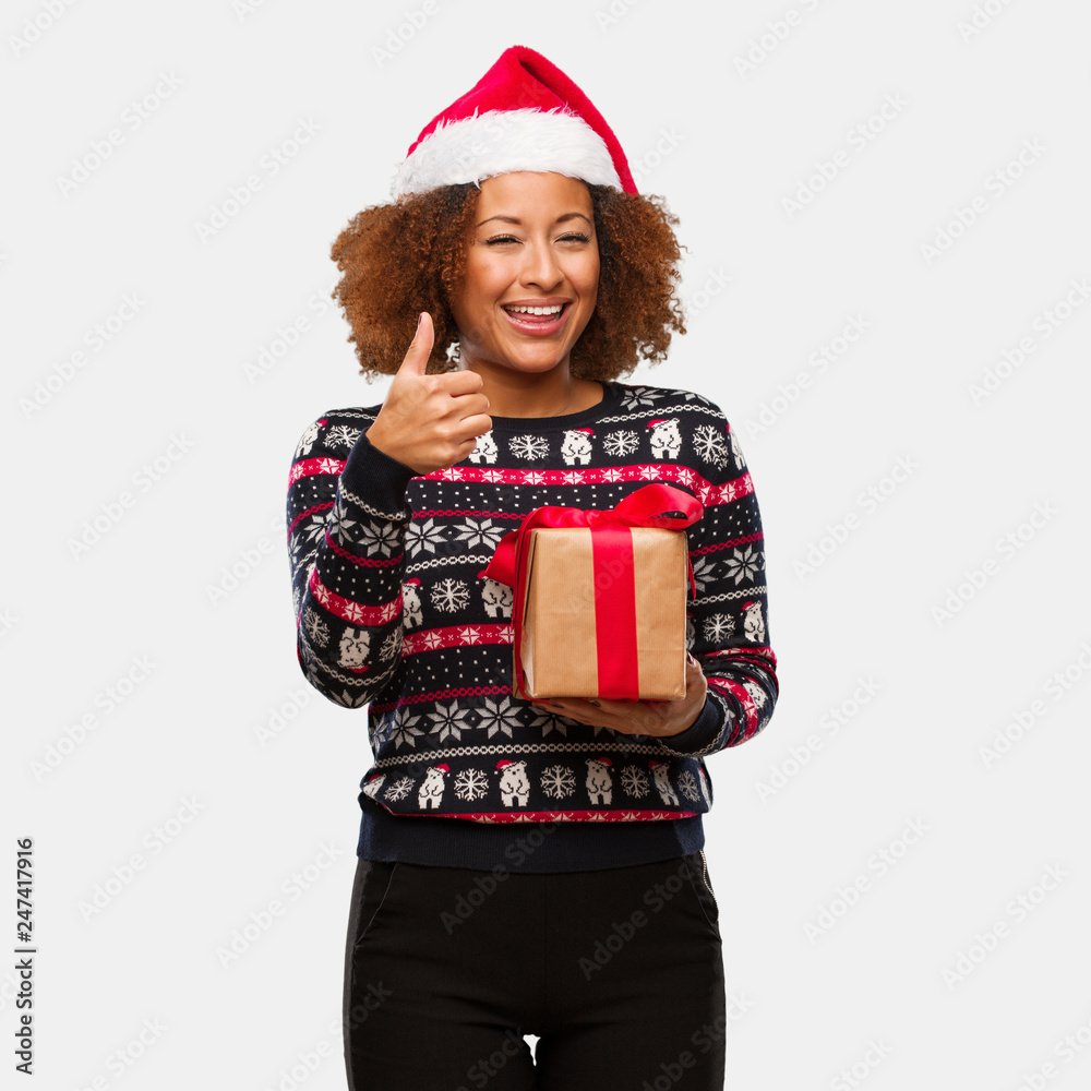 Young black woman holding a gift in christmas day smiling and raising thumb up Young black woman holding a gift in christmas day smiling and raising thumb up