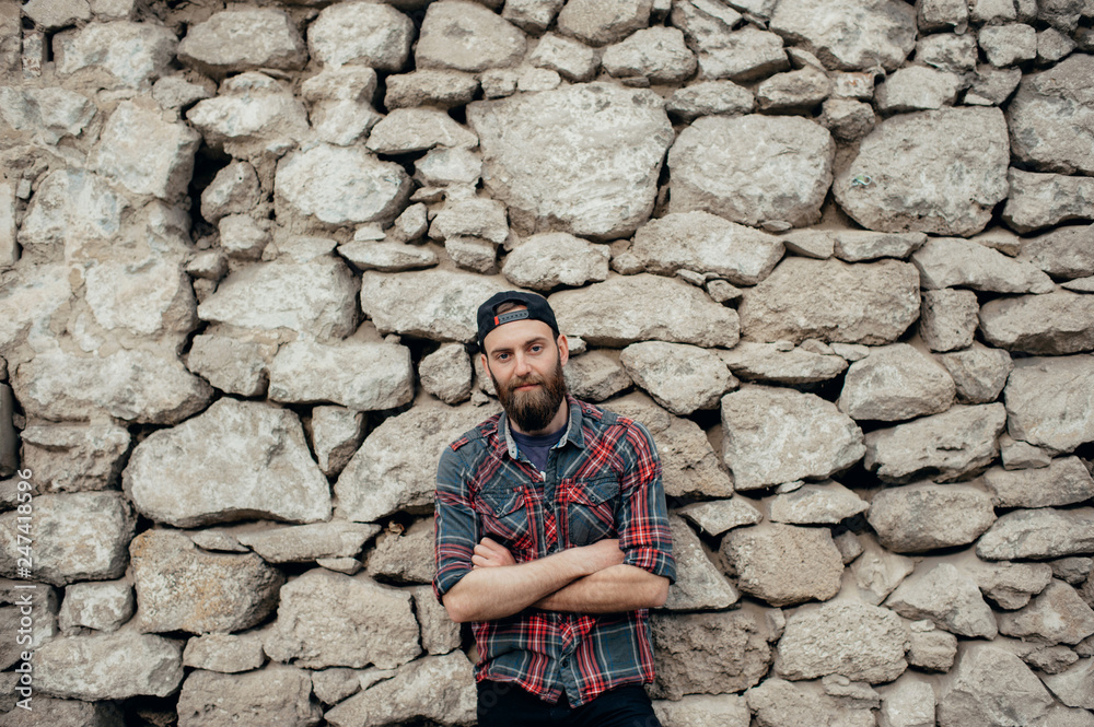 Image of serious man with arms folded standing over stone wall and looking at camera Image of serious man with arms folded standing over stone wall and looking at camera