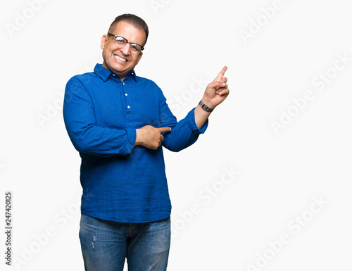 Middle age arab man wearing glasses over isolated background with a big smile on face, pointing with hand and finger to the side looking at the camera.