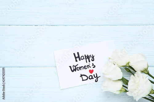 Text Happy Women's Day with eustoma flowers on wooden table