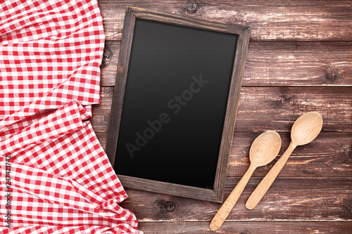 Blank chalkboard with red napkin and spoons on wooden background