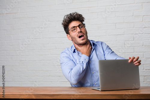 Photos Young business man sitting and working on a laptop worried and overwhelmed, anxi