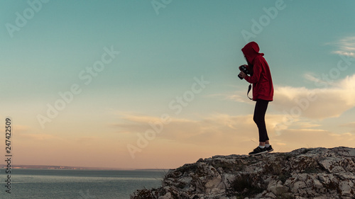 A girl stands and takes photos on a precipice of mountain against the background of a beautiful sky