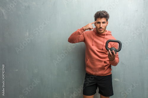 Young fitness man against a grunge wall man making a concentration gesture, looking straight ahead focused on a goal. Holding an iron dumbbell. photo