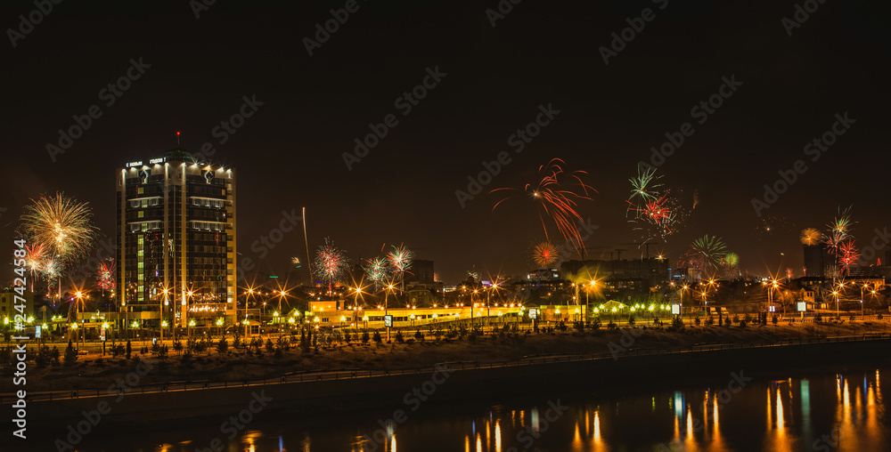 panorama of fireworks over the night city reflected in the river