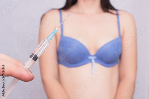 Female breast augmentation with hyaluronic acid injection, the doctor holds a syringe with hiluric acid on the background of the girl's bust photo