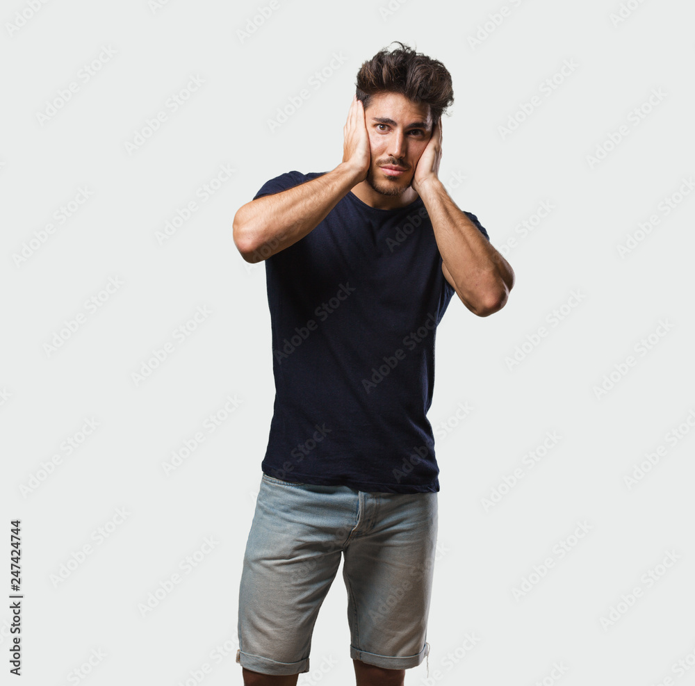 Young handsome man standing covering ears with hands, angry and tired of hearing some sound Young handsome man standing covering ears with hands, angry and tired of hearing some sound