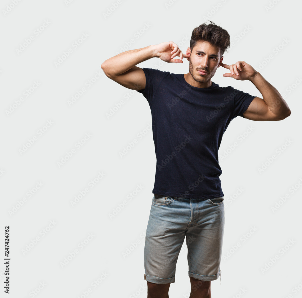 Young handsome man standing covering ears with hands, angry and tired of hearing some sound Young handsome man standing covering ears with hands, angry and tired of hearing some sound