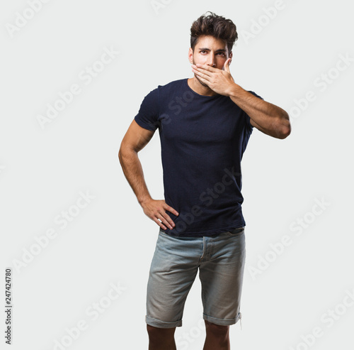 Young handsome man standing covering mouth, symbol of silence and repression, trying not to say anything