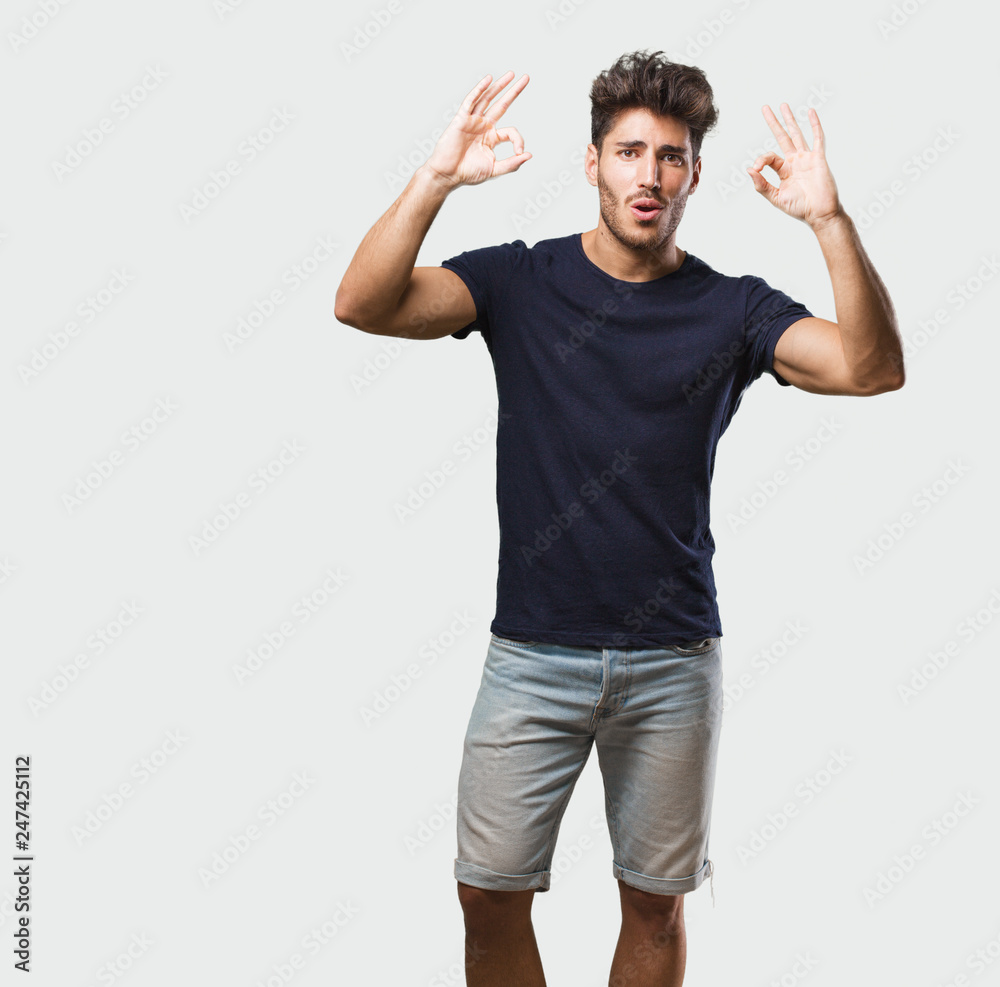 Young handsome man standing cheerful and confident doing ok gesture, excited and screaming, concept of approval and success Young handsome man standing cheerful and confident doing ok gesture, excited and screaming, concept of approval and success
