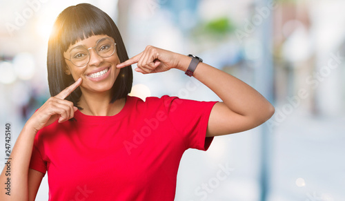 Beautiful young african american woman wearing glasses over isolated background smiling confident showing and pointing with fingers teeth and mouth. Health concept.
