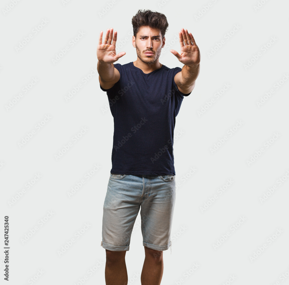 Young handsome man standing serious and determined, putting hand in front, stop gesture, deny concept Young handsome man standing serious and determined, putting hand in front, stop gesture, deny concept