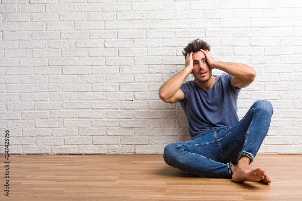 Young natural man sit on a wooden floor frustrated and desperate, angry and sad with hands on head Young natural man sit on a wooden floor frustrated and desperate, angry and sad with hands on head