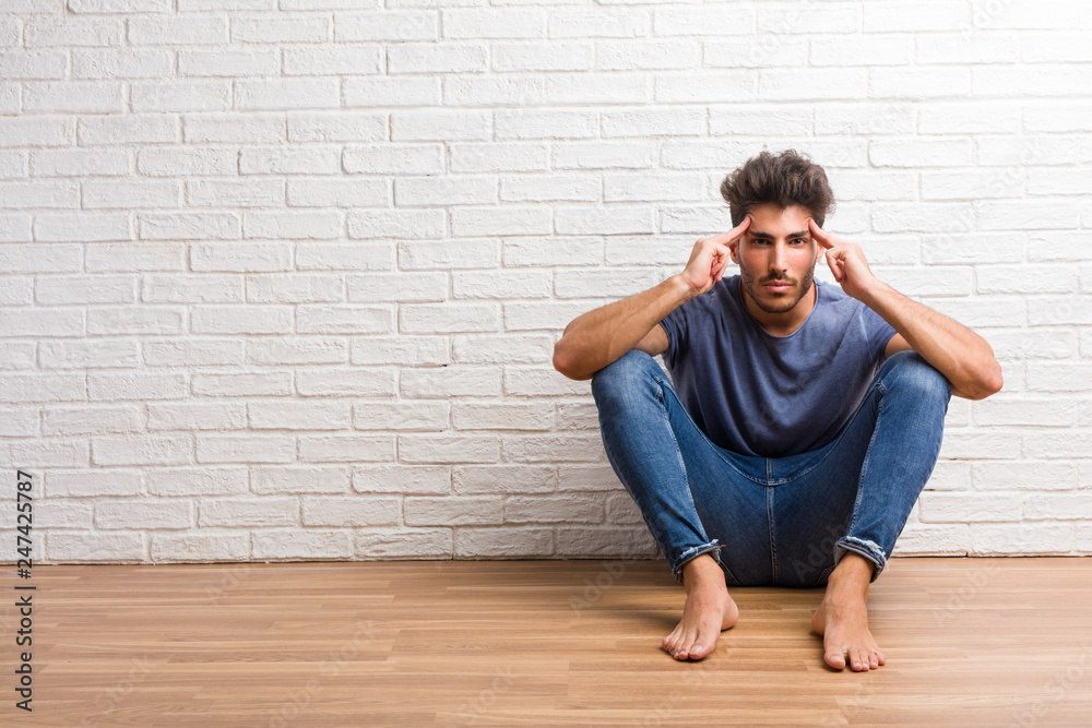 Young natural man sit on a wooden floor man making a concentration gesture, looking straight ahead focused on a goal Young natural man sit on a wooden floor man making a concentration gesture, looking straight ahead focused on a goal