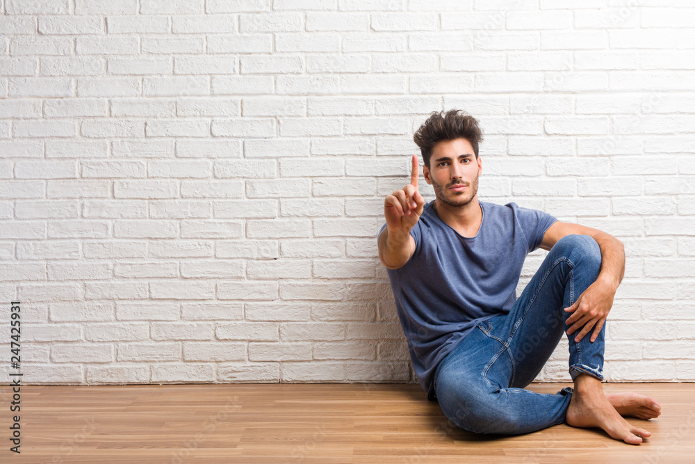 Young natural man sit on a wooden floor showing number one, symbol of counting, concept of mathematics, confident and cheerful Young natural man sit on a wooden floor showing number one, symbol of counting, concept of mathematics, confident and cheerful