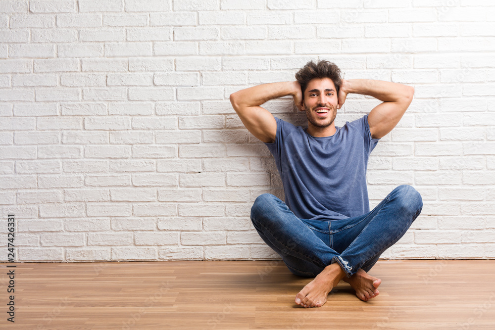 Young natural man sit on a wooden floor surprised and shocked, looking with wide eyes, excited by an offer or by a new job, win concept Young natural man sit on a wooden floor surprised and shocked, looking with wide eyes, excited by an offer or by a new job, win concept