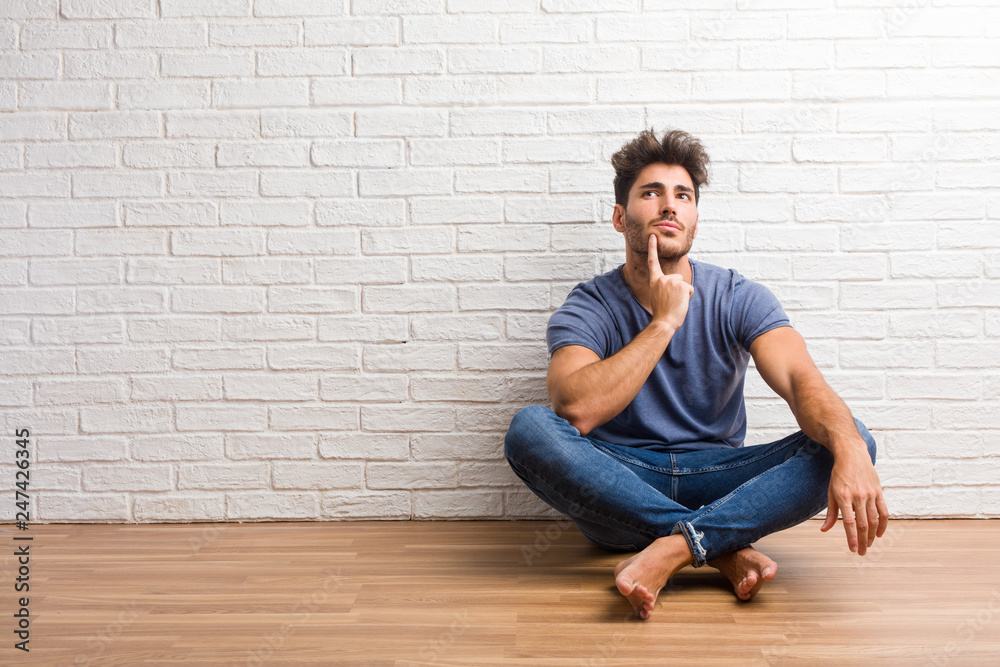 Young natural man sit on a wooden floor thinking and looking up, confused about an idea, would be trying to find a solution Young natural man sit on a wooden floor thinking and looking up, confused about an idea, would be trying to find a solution