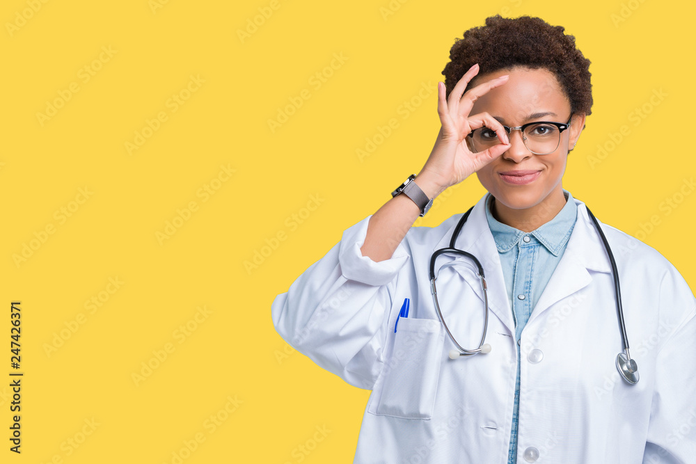 Young african american doctor woman wearing medical coat over isolated background doing ok gesture with hand smiling, eye looking through fingers with happy face.