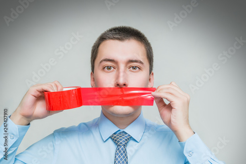 man with wrapping adhesive tape around mouth. Businessman silenced with duct tape over his mouth. Frightened man covered mouth with red insulating tape