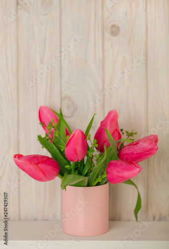 Spring bouquet of pink tulips with branches of a blossoming tree on a light wooden background.