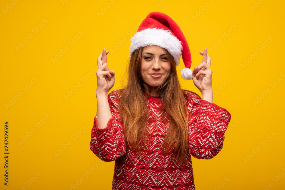 Young woman wearing santa hat crossing fingers for having luck Young woman wearing santa hat crossing fingers for having luck