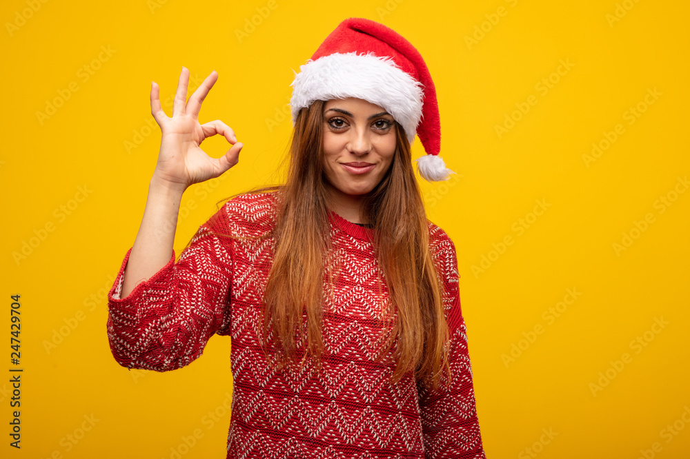 Young woman wearing santa hat cheerful and confident doing ok gesture Young woman wearing santa hat cheerful and confident doing ok gesture