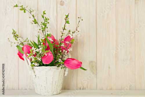 Spring bouquet of pink tulips with branches of a blossoming tree on a light wooden background.