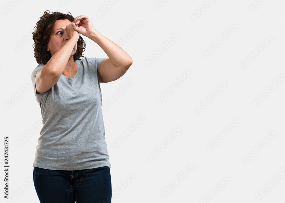 Middle aged woman looking through a gap, hiding and squinting Middle aged woman looking through a gap, hiding and squinting