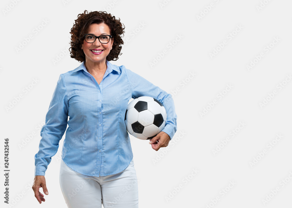 Middle aged woman smiling and happy, holding a soccer ball, competitive attitude, excited to play a game
