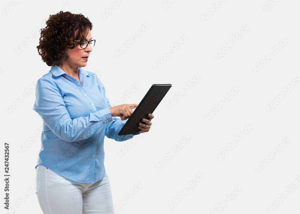 Middle aged woman smiling and confident, holding a tablet, using it to surf the internet and see social networks, communication concept Middle aged woman smiling and confident, holding a tablet, using it to surf the internet and see social networks, communication concept
