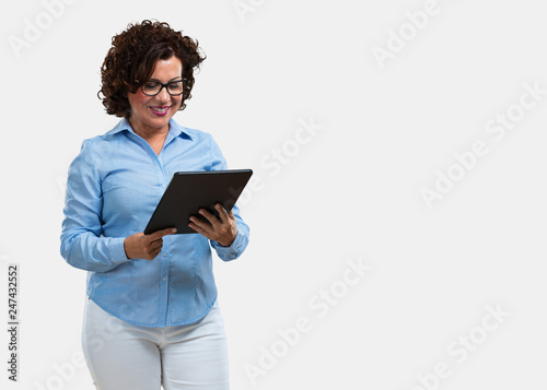 Wallpaper Mural Middle aged woman smiling and confident, holding a tablet, using it to surf the internet and see social networks, communication concept Torontodigital.ca