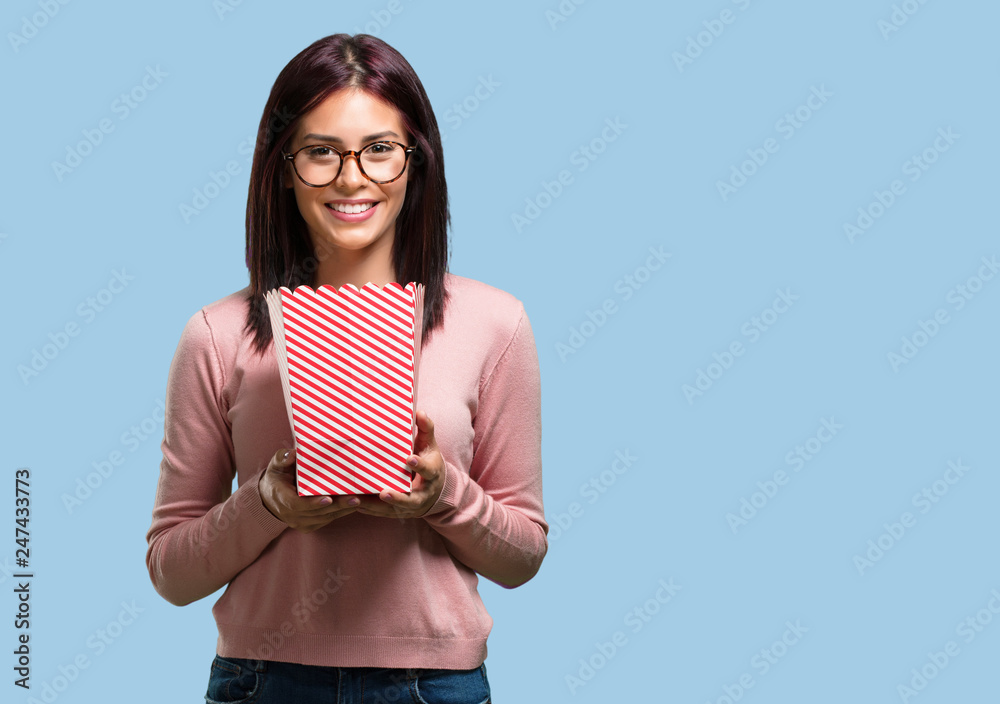 Young pretty woman happy and fascinated, holding a striped popcorn bucket, surprised by the new movie, eyes open and expression of admiration Young pretty woman happy and fascinated, holding a striped popcorn bucket, surprised by the new movie, eyes open and expression of admiration