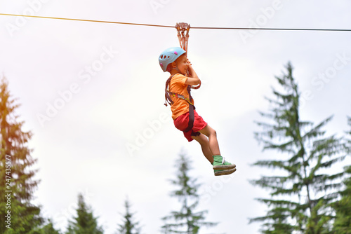 Happy kid with helmet and harness on zip line between trees