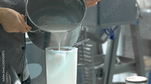 Worker pouring milk into container. Woman pouring milk from pan into plastic container, cropped image. Dairy industry concept.