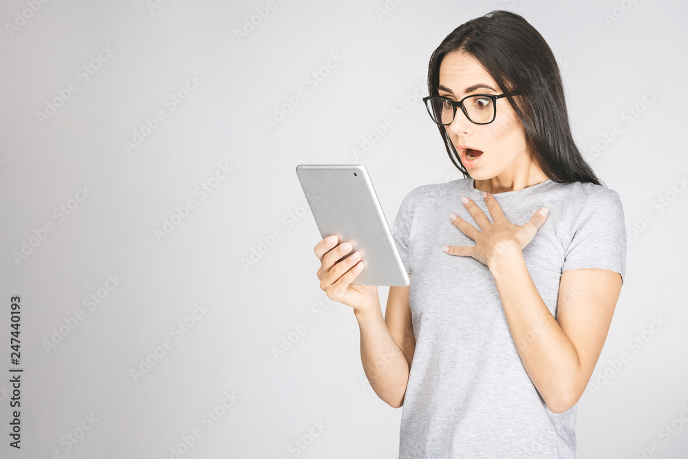 Picture of surprised young brunette woman wearing glasses standing isolated over white wall. Chatting by tablet computer. Picture of surprised young brunette woman wearing glasses standing isolated over white wall. Chatting by tablet computer.