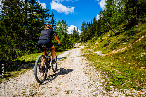 Tourist cycling in Cortina d'Ampezzo, stunning rocky mountains on the background. Woman riding MTB enduro flow trail. South Tyrol province of Italy, Dolomites.