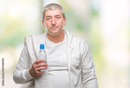 Handsome senior man training holding towel and water bottle over isolated background with a confident expression on smart face thinking serious