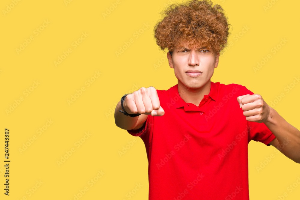 Young handsome man with afro hair wearing red t-shirt Punching fist to fight, aggressive and angry attack, threat and violence Young handsome man with afro hair wearing red t-shirt Punching fist to fight, aggressive and angry attack, threat and violence