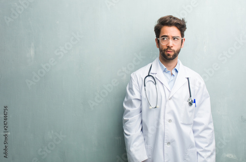Young friendly doctor man against a grunge wall with a copy space doubting and confused, thinking of an idea or worried about something