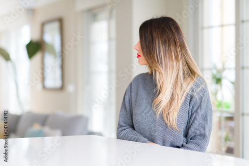 Young beautiful woman wearing winter sweater at home looking to side, relax profile pose with natural face with confident smile.