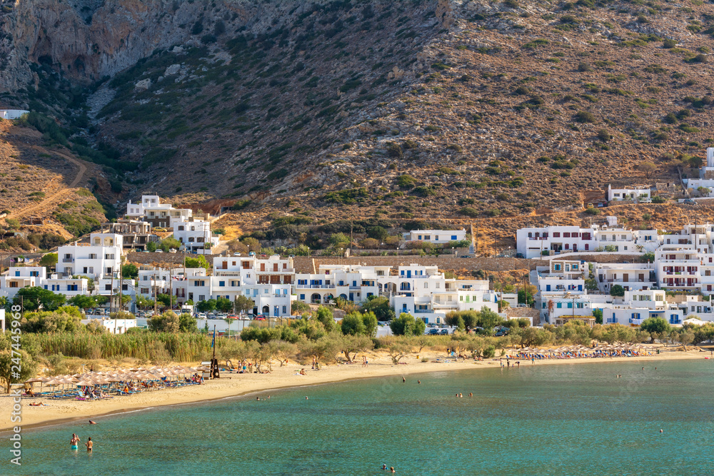 Sandy beach with clean emerald water on the background of Kamares buildings. The island of Sifnos from the Cycladic group. Greece